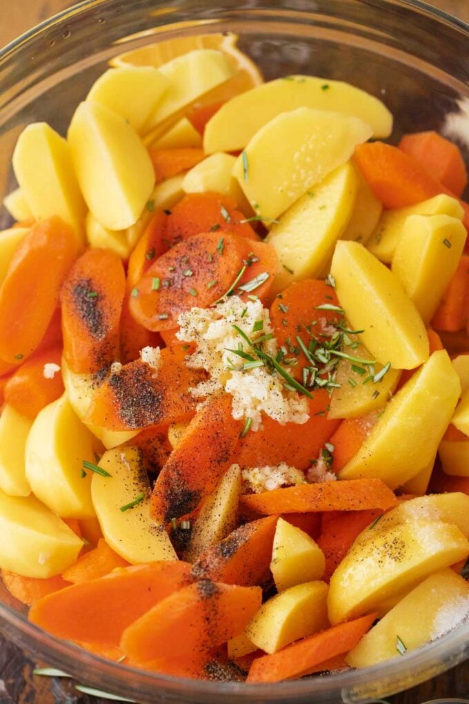 A bowl of chopped carrots and potatoes with seasonings.