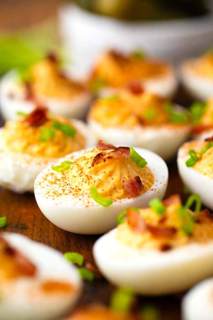 classic deviled eggs arranged on a serving board, topped with paprika and bacon