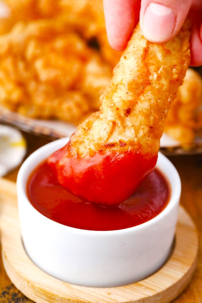 Dipping golden chicken in ketchup.