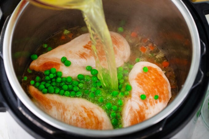 Pouring broth over chicken breasts and sweet peas in the Instant Pot.