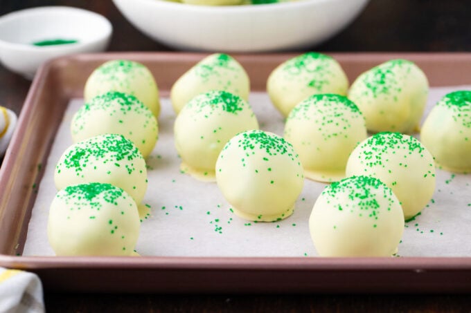 Homemade mint chocolate chip truffles topped with green sanding sugar on a baking sheet.
