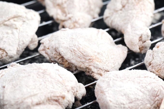 Flour coated chicken pieces resting on a wire rack.