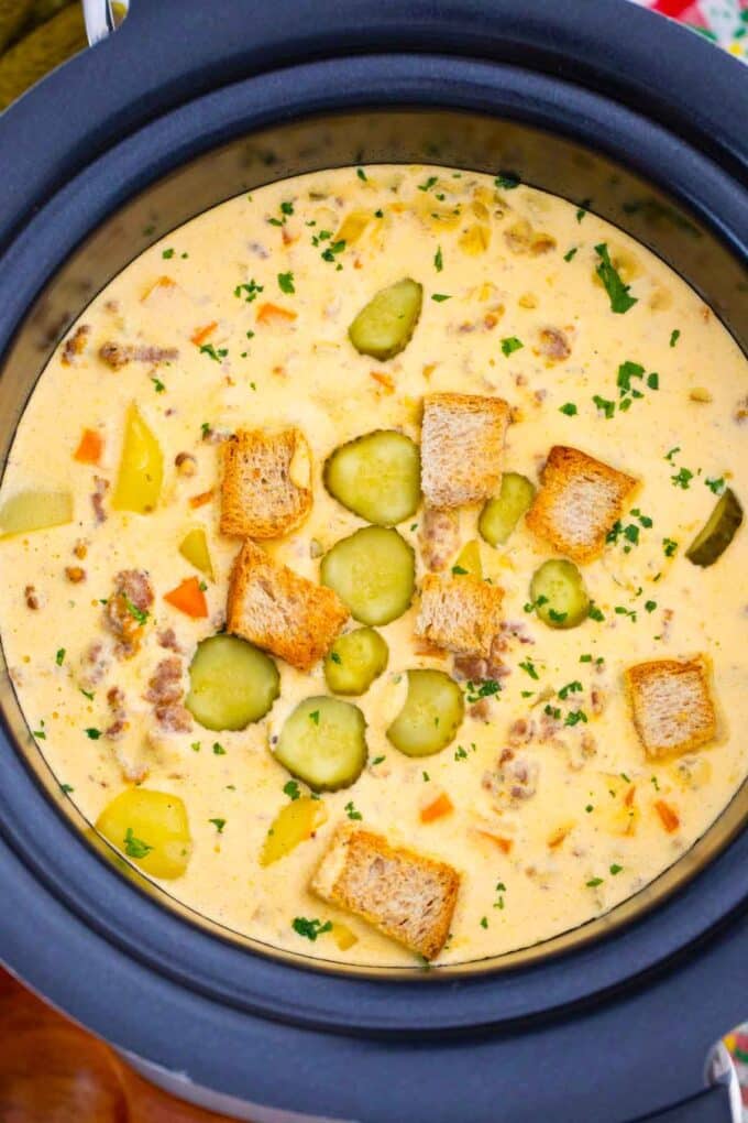 overhead shot of a bowl of slow cooker cheeseburger soup topped with croutons and pickles in a crockpot