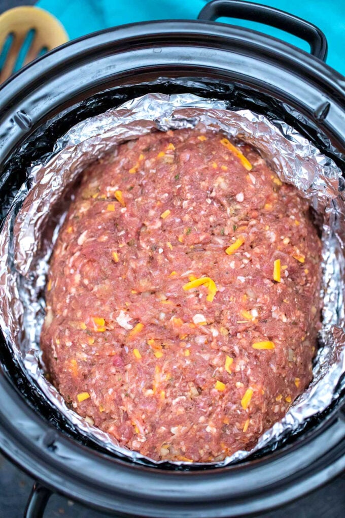Shaped meatloaf in aluminum foil put in the crockpot for cooking.