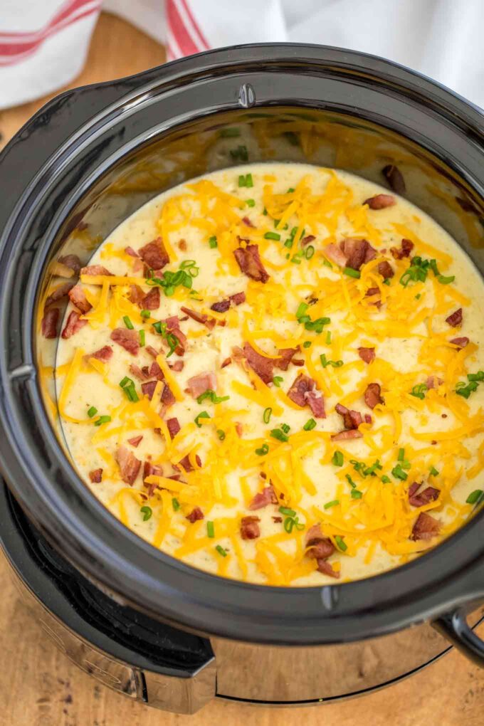 Crockpot cheesy potato soup topped with shredded cheddar cheese and bacon