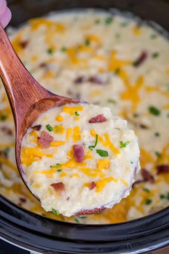 Slow cooker potato soup with cheddar cheese and bacon bits on a wooden spoon