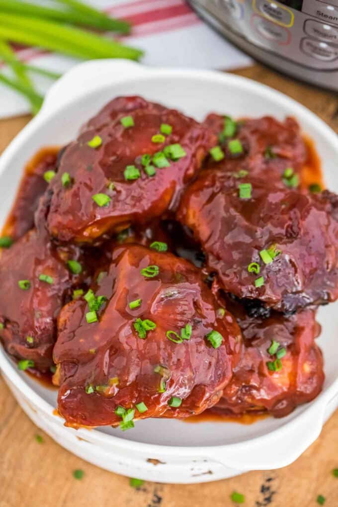 Photo of instant pot BBQ chicken garnished with chopped green onion on a white plate.