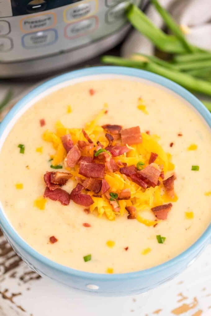 Picture of cheesy potato soup garnished with bacon and shredded cheese.