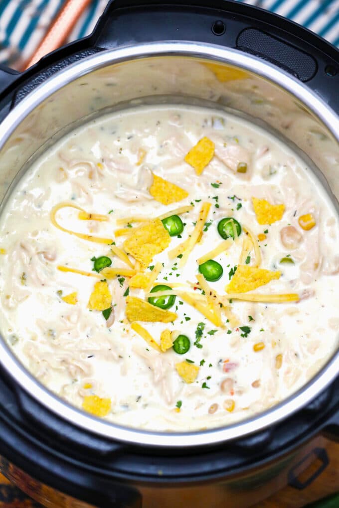 Photo of instant pot white chicken chili topped with tortilla chips and sliced jalapeno. 