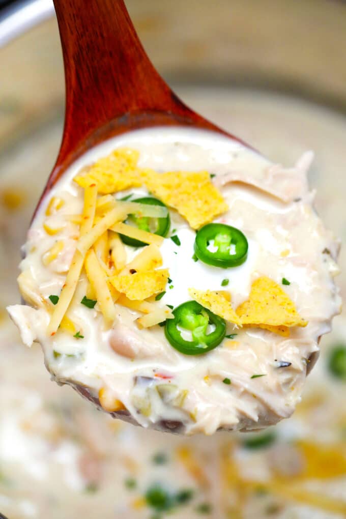 Image of white chicken chili garnished with tortilla chips and sliced jalapeno on a wooden spoon.