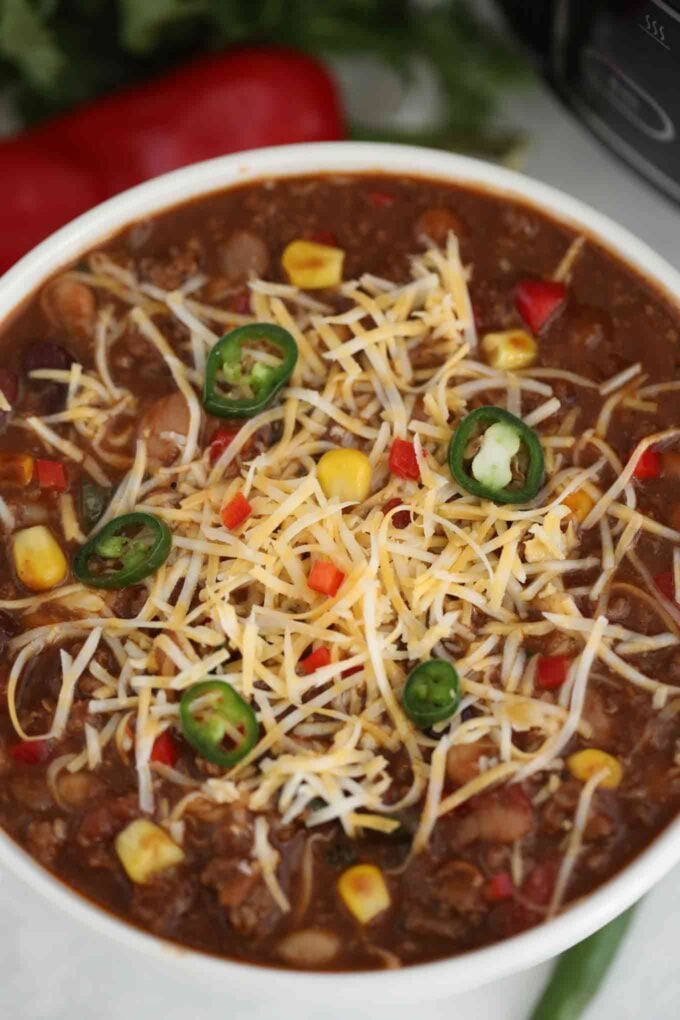 classic slow cooker chili in a white bowl topped with shredded cheese and chopped jalapenos 