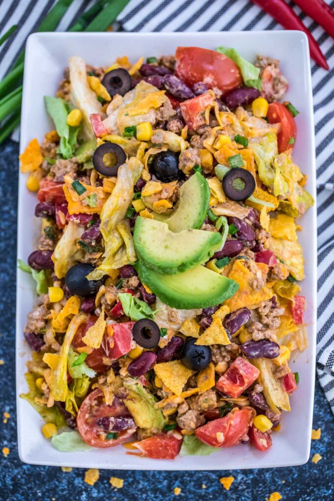 Taco salad with lettuce beans veggies olives in a creamy dressing topped with avocado slices