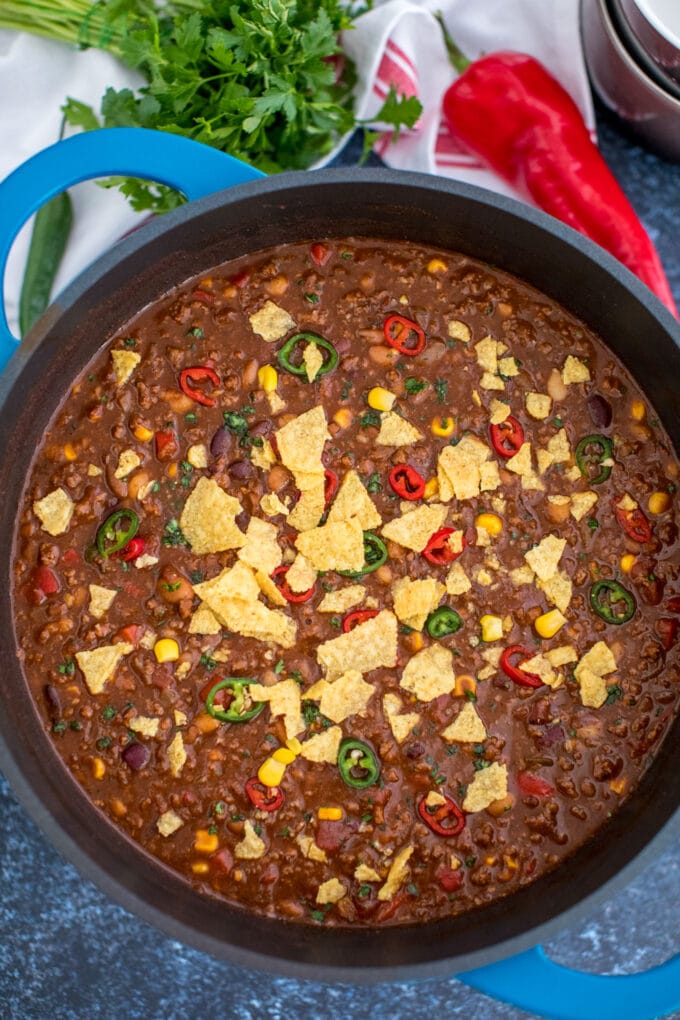 Classic chili recipe in a large Dutch oven topped with crashed chips and chopped jalapenos 