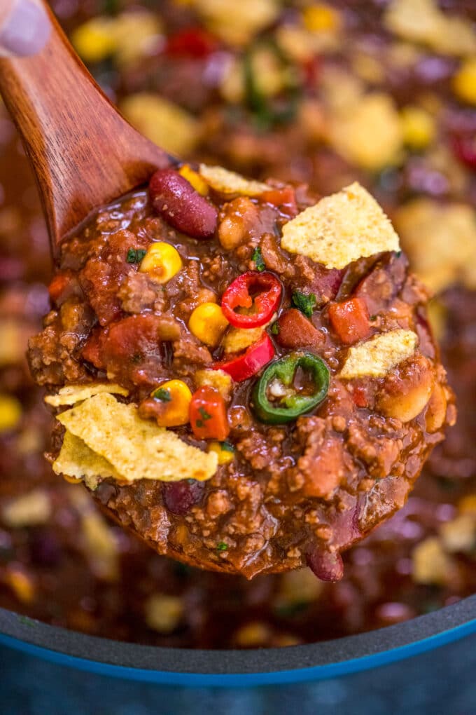 A spoonful of beef chili garnished with sweet corn, chili peppers, and chips.