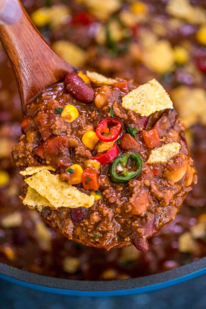 A spoonful of beef chili garnished with sweet corn, chili peppers, and chips. 