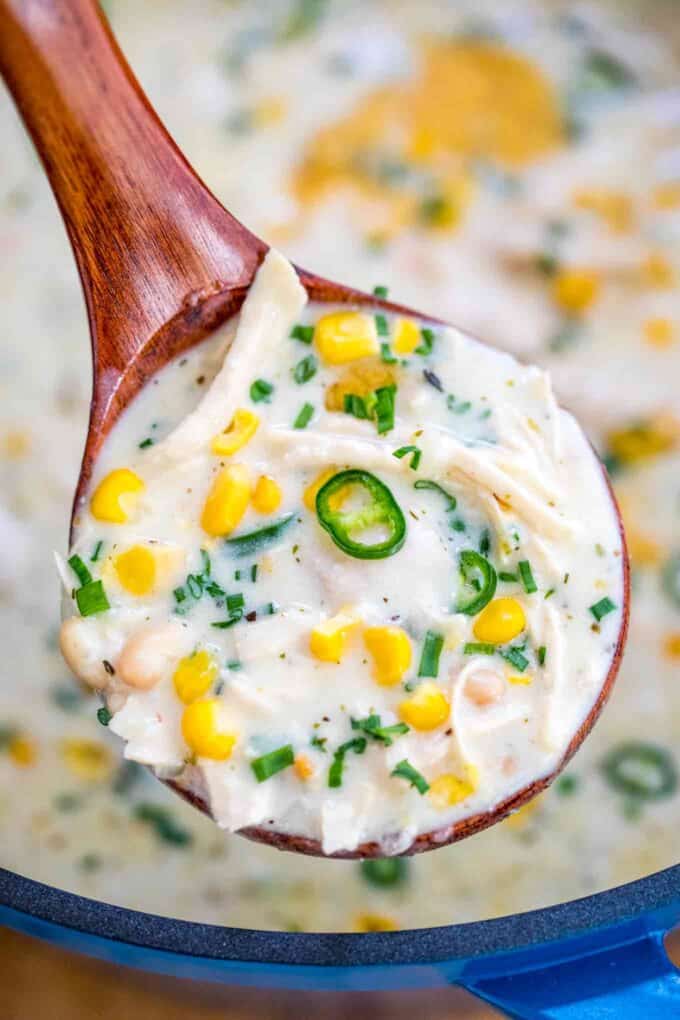 A spoonful of white beans chicken chili garnished with corn and chopped jalapeno.