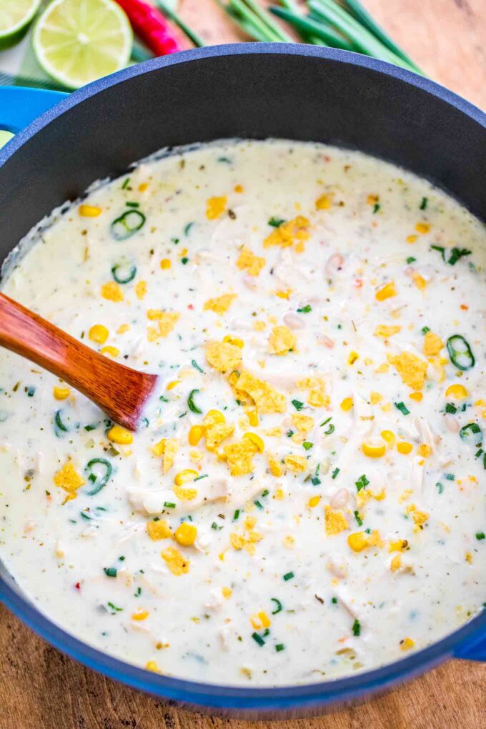 White chicken chili in a large Dutch oven topped with crushed chips and chopped jalapeno