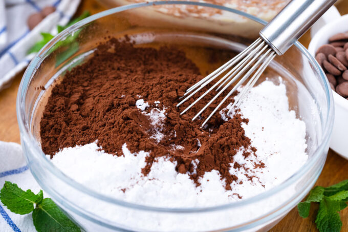 Adding powdered sugar and cocoa powder to chocolate frosting.