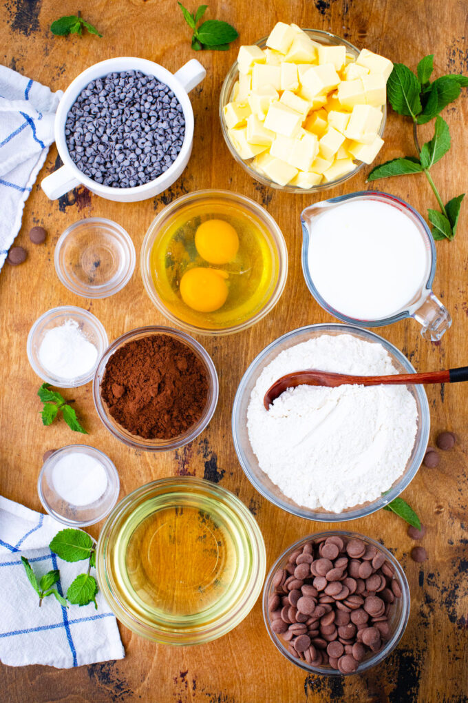 Overhead shot of mint chocolate chip cake ingredients in bowls on a wooden surface.