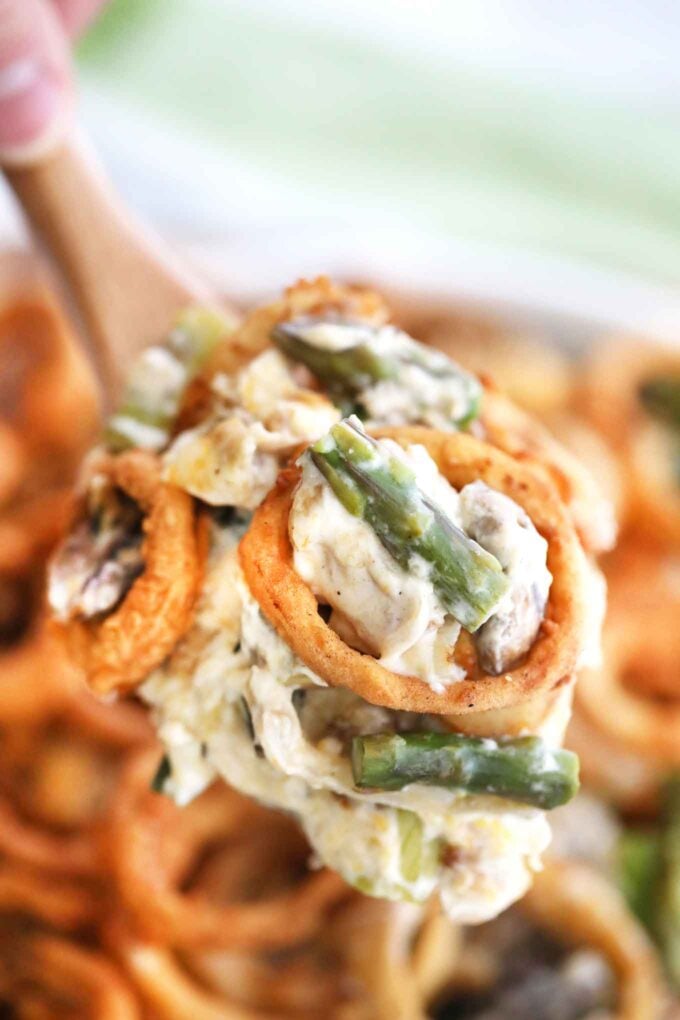 Cheesy asparagus casserole with French fried onions on a wooden spoon