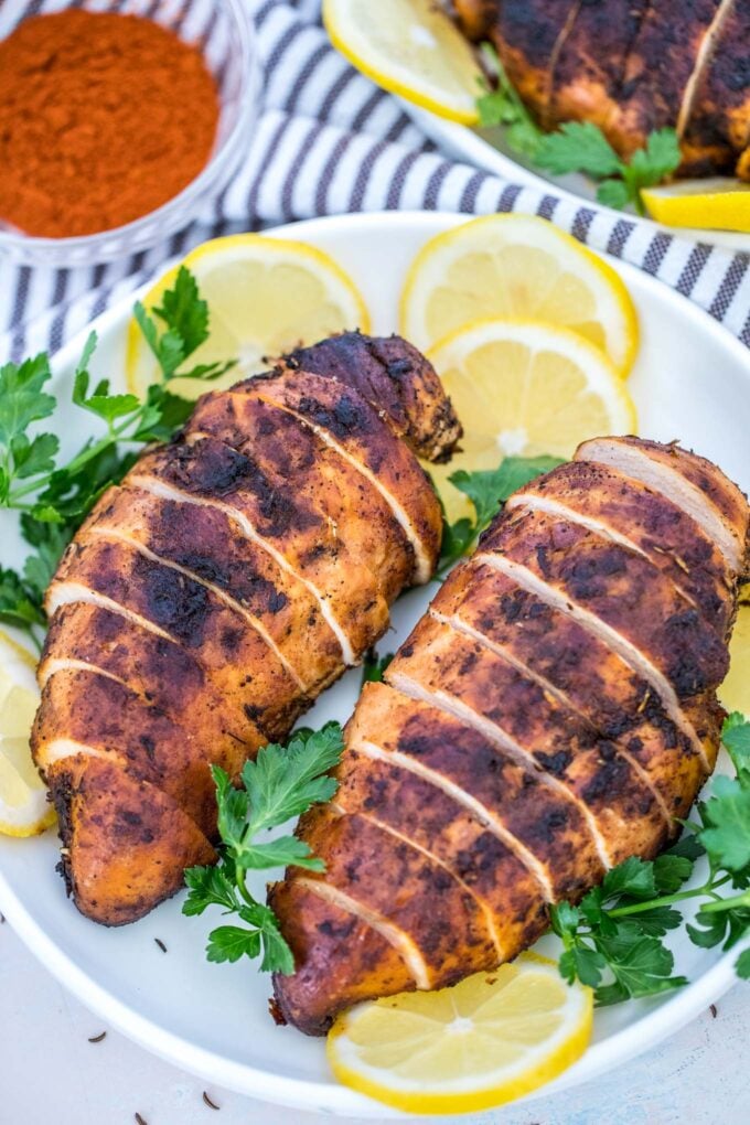 Blackened chicken breasts with sliced lemon on a plate. 