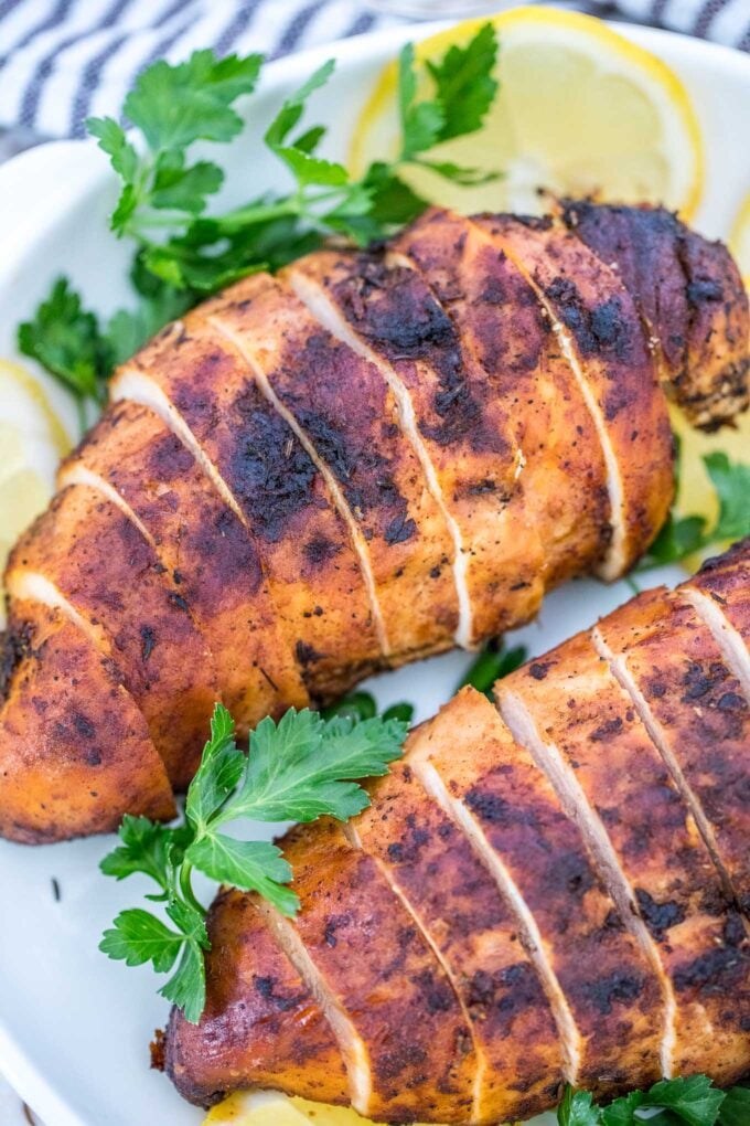 Sliced blackened chicken breasts with lemon and parsley on a white plate. 