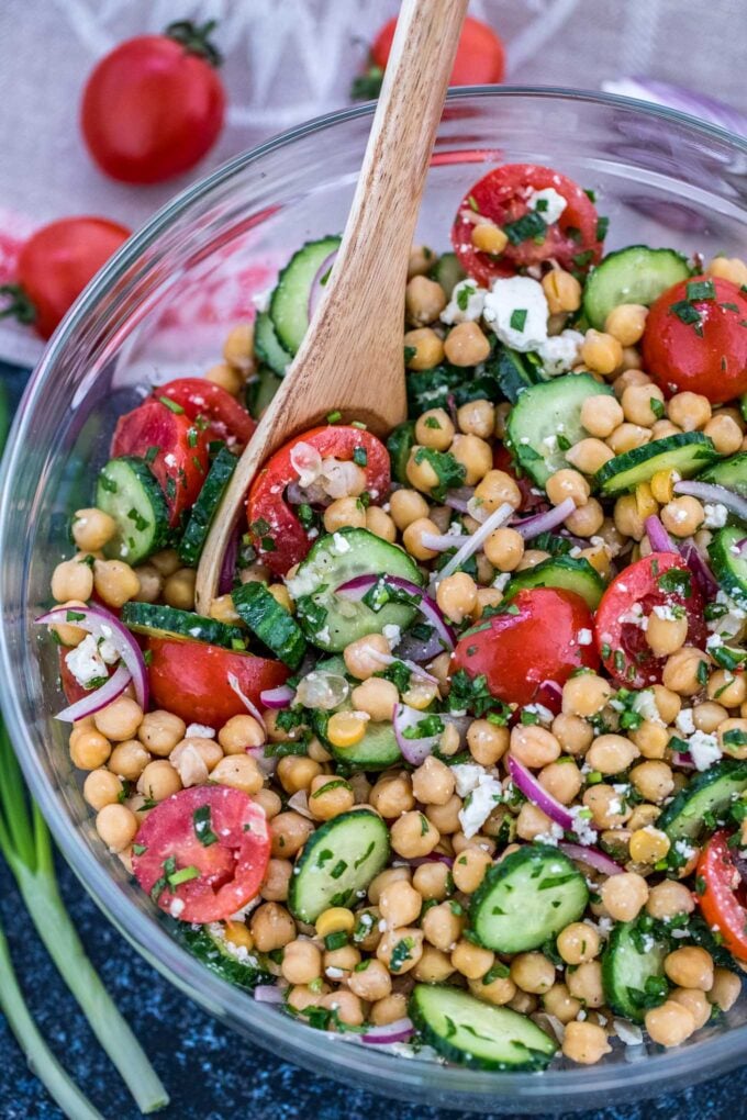 A large bowl of freshly cut salad made with chickpeas, cucumber, avocado, tomatoes, and onions.