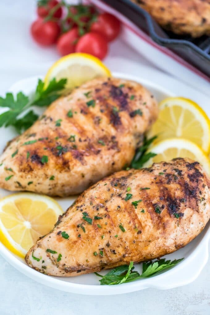 Grilled chicken breasts in a plate with fresh lemon slices and parsley