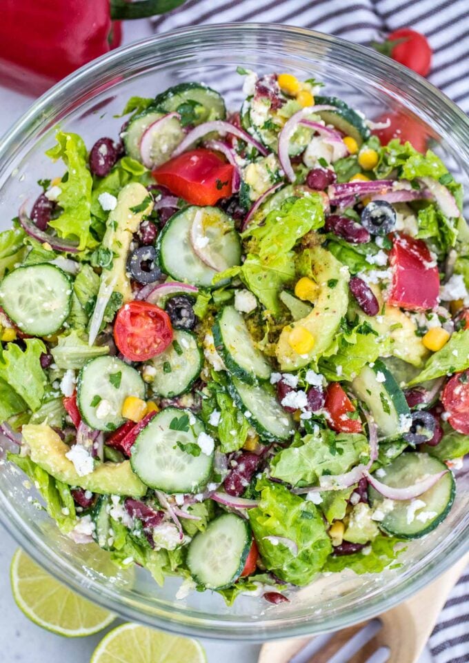 Vegetarian salad made with black beans, lettuce, cucumber, avocado, red onion, corn and cilantro in a glass bowl