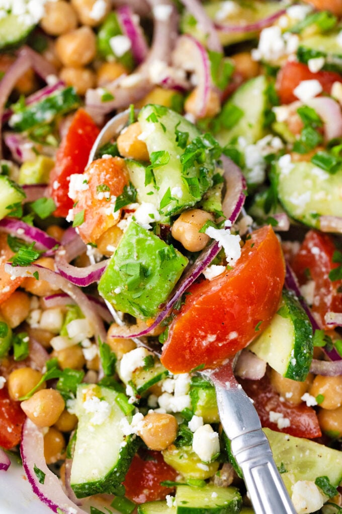 Close shot of a spoonful of chickpea salad with avocado, cucumbers, and tomatoes.