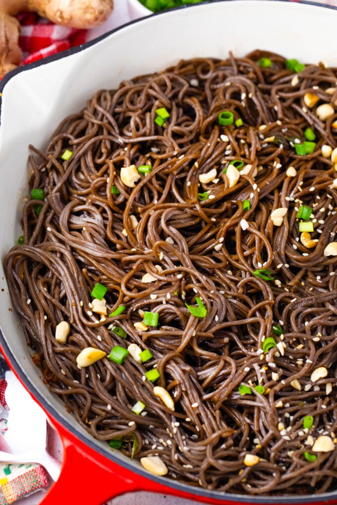 A skillet of homemade soba noodles in sweet and savory sauce, topped with chopped peanuts and green onions.