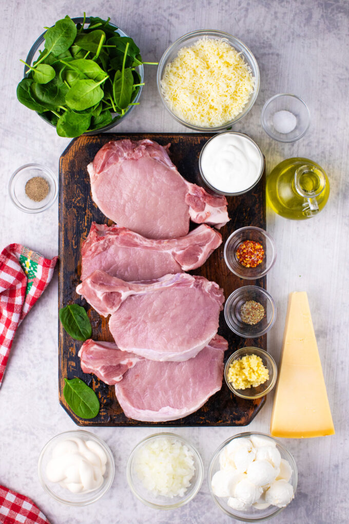 Overhead shot of cheesy spinach dip stuffed pork chops ingredients arranged on a white surface.