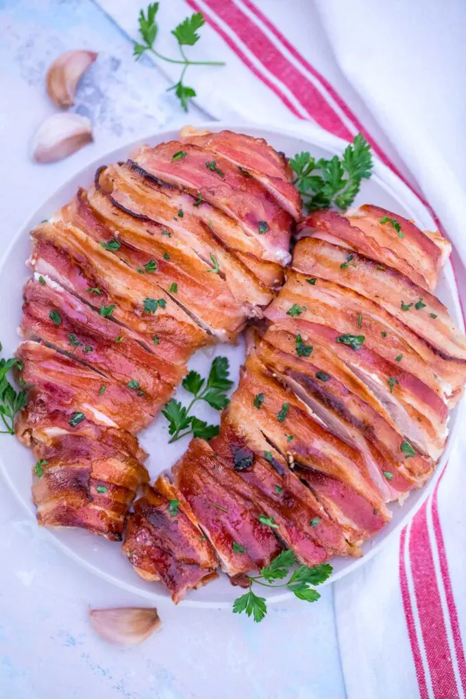 Picture of bacon wrapped cream cheese stuffed chicken garnished with chopped parsley.