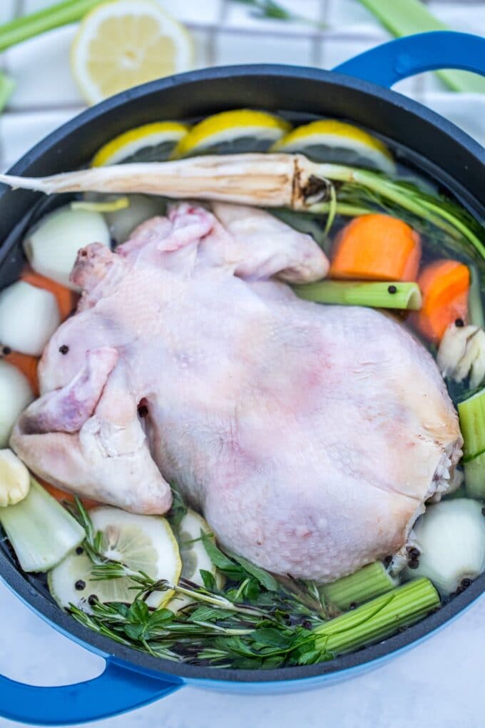 Whole chicken in a pot with herbs and veggies.