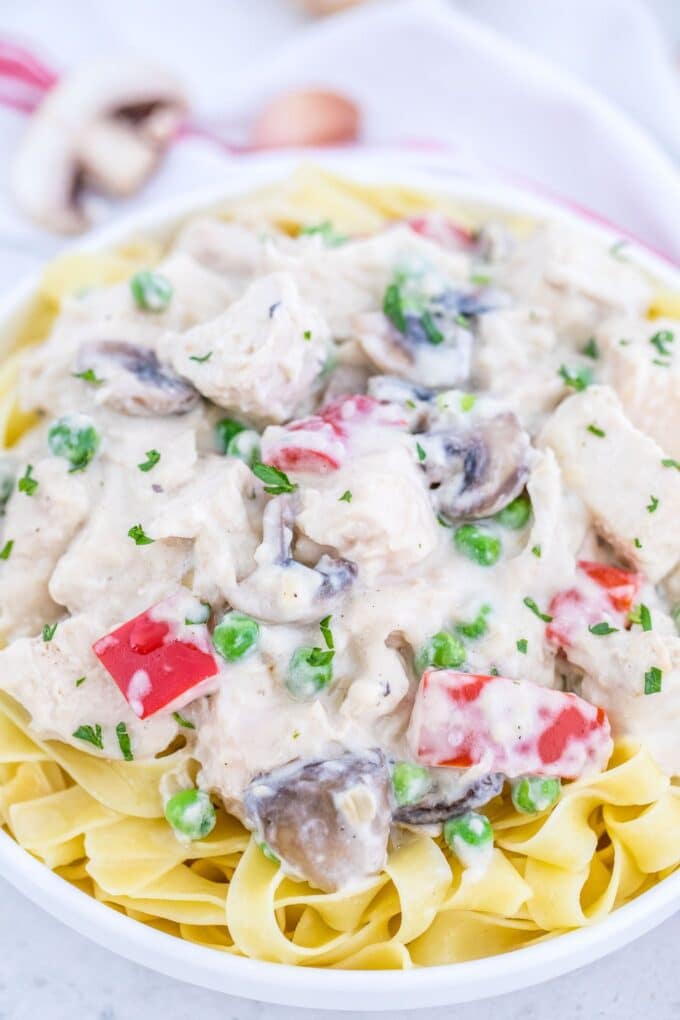 Tender chicken in a creamy sauce with mushrooms, bell peppers and peas over pasta