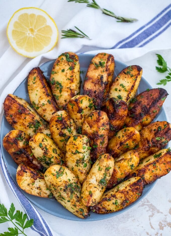 Grilled potato wedges garnished with chopped parsley and lemon on a blue plate.