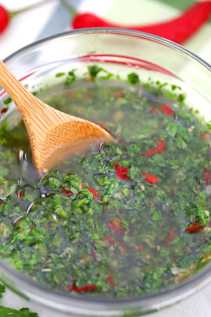 a bowl of fresh chimichurri sauce with a wooden spoon in it