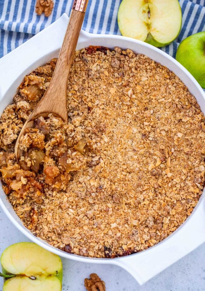 Classic Apple Crumble topped with a layer of crispy oats, with a wooden spoon in it showing the juicy apple pieces