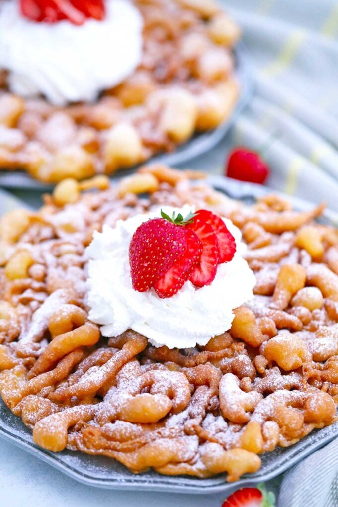 Image of funnel cake topped with whipped cream and sliced strawberry.