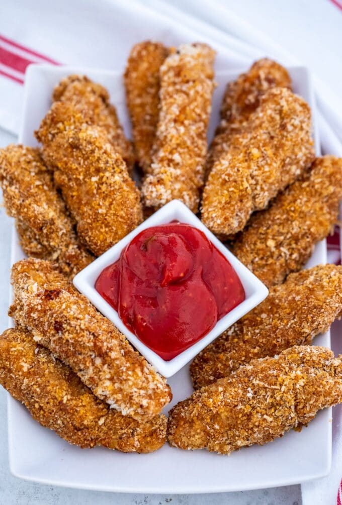 Crunchy baked chicken tenders piled on a plate with a side of ketchup.