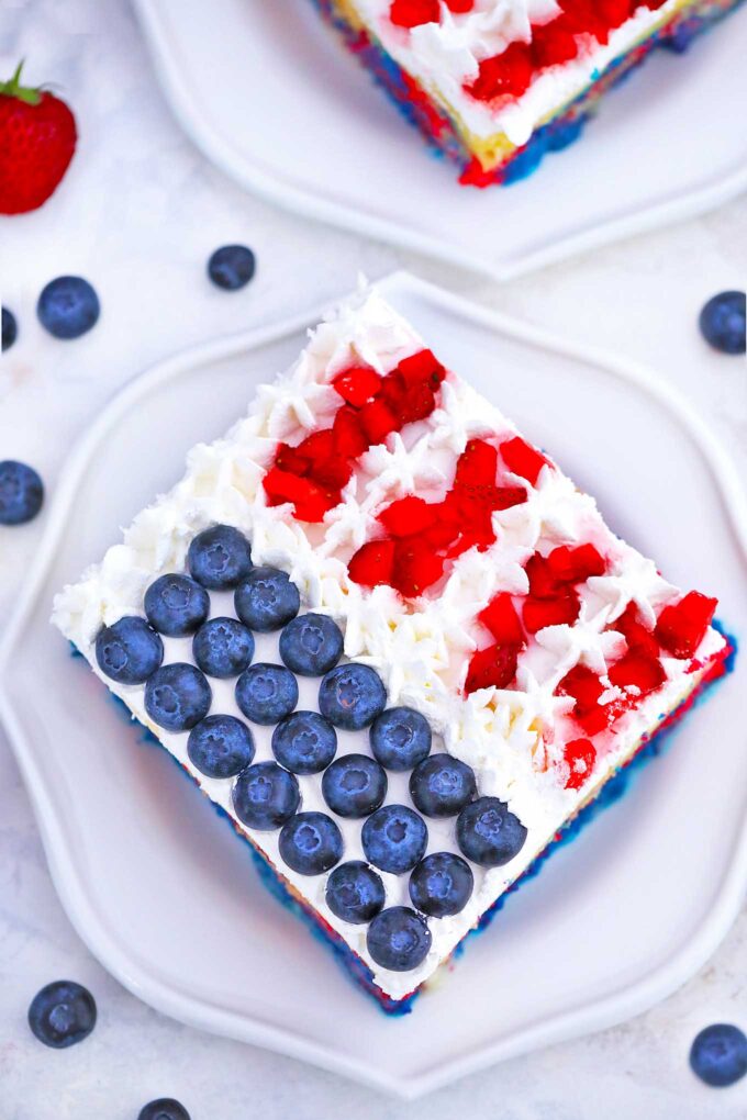 a slice of red white ad blue Patriotic Poke Cake topped with fresh blueberries and strawberries