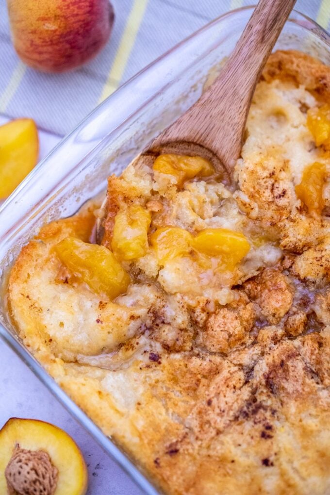 Homemade peach cobbler in a baking dish with a serving spoon