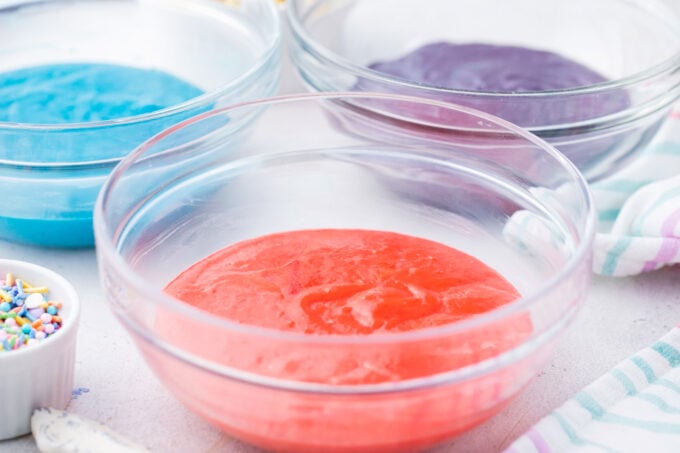 Pink, light blue, and purple cake batter in bowls.