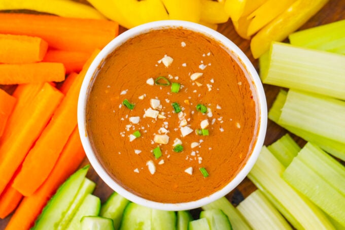 Overhead shot of creamy peanut sauce with veggies sticks around it.