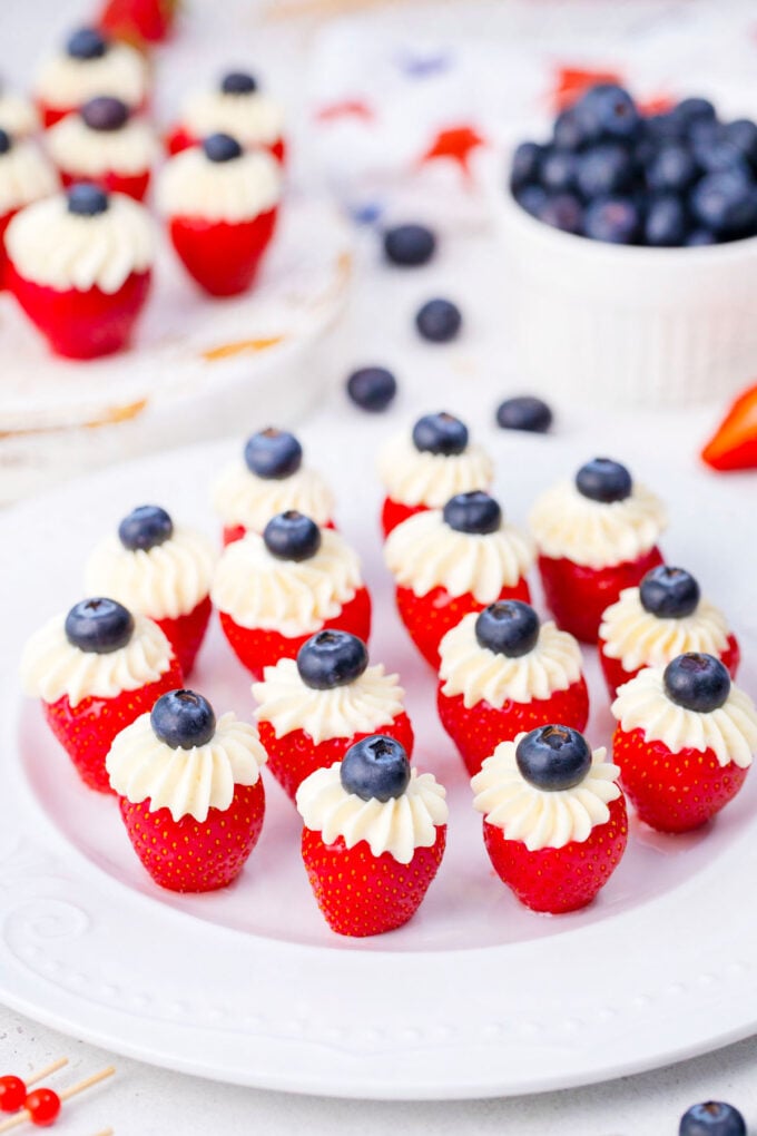 A serving plate of cream cheese stuffed strawberries topped with blueberries.