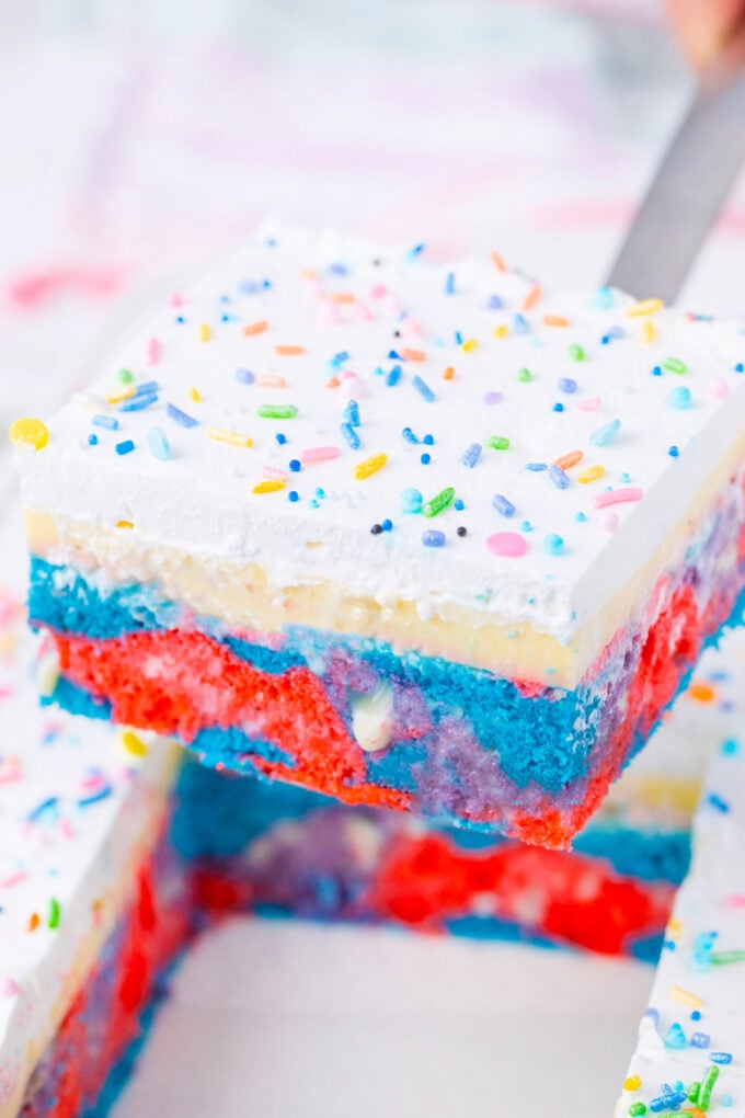 A slice of unicorn poke cake topped with sprinkles.