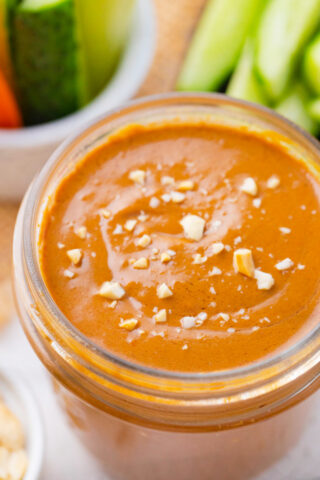 A jar of asian creamy peanut sauce topped with chopped peanuts.