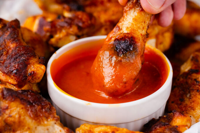Dipping crisp grilled chicken wings in homemade buffalo sauce.