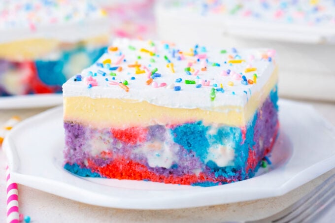 A slice of pink, blue, and purple unicorn poke cake with sprinkles.