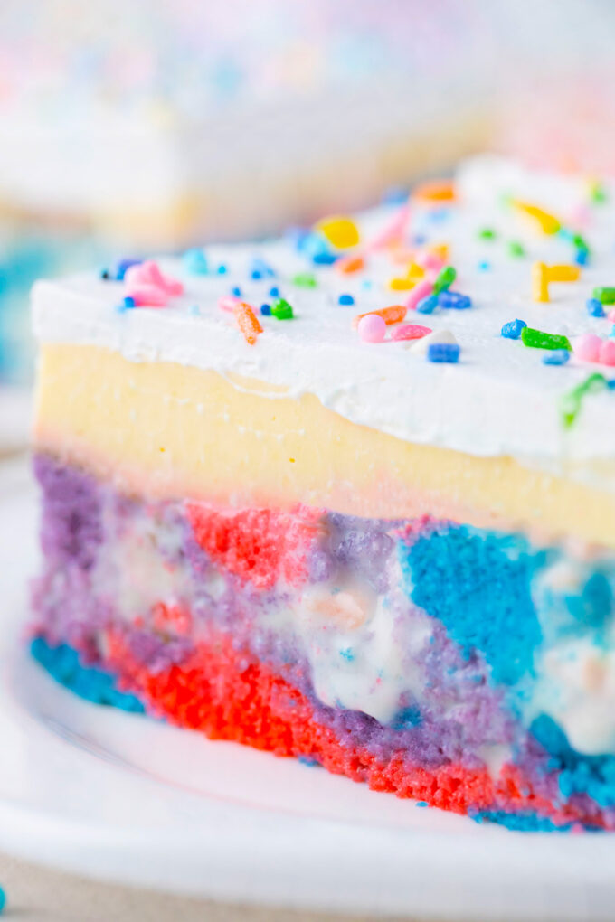 Close shot of unicorn poke cake with pudding and whipped cream.